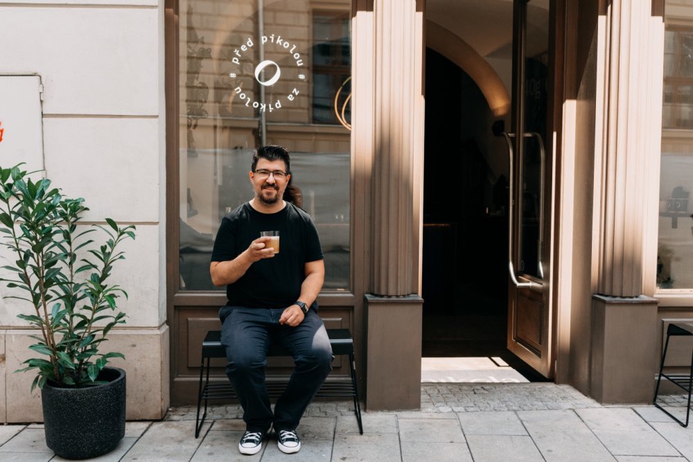 Martin Kopa sedí na lavičce před Pikolou a v ruce má flat white