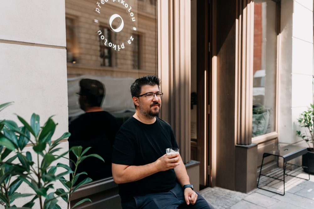 Martin Kopa sedí před kavárnou Pikola a vychutnává si svůj flat white
