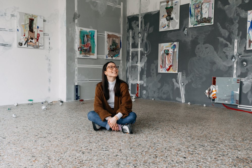 Tereza Dehnerová sedí v tureckém sedu na zemi v ateliéru, kouká do strany a usmívá se