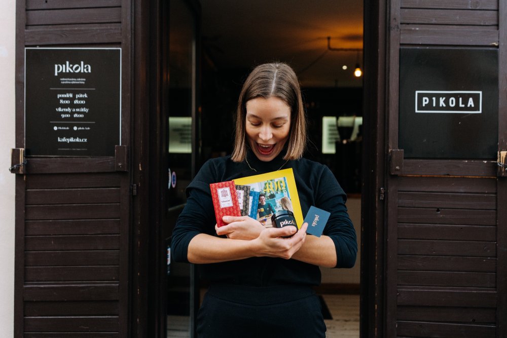 Čokolády Ajala a další dárky od Pikoly v rukách slečny, která stojí ve dveřích šumperské kavárny Pikola a raduje se